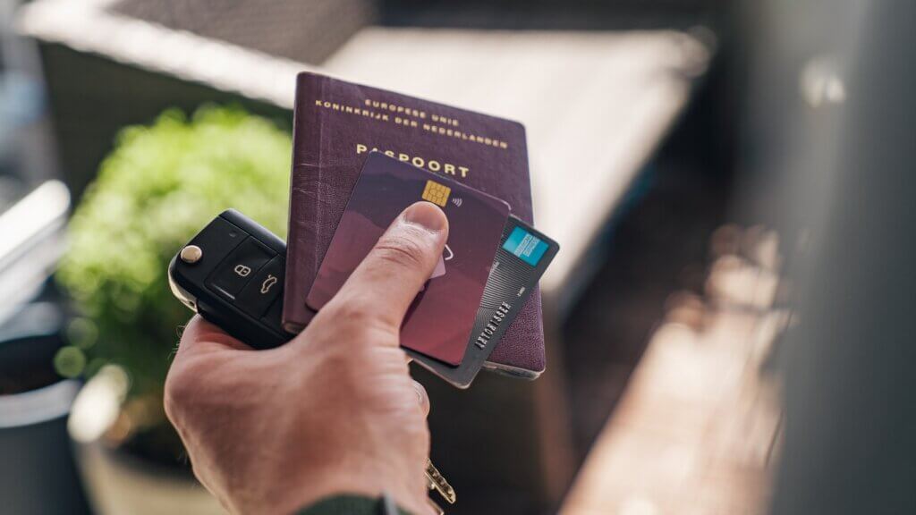 person holding credit cards, car key and passport
